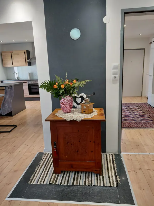 Corridor with a wooden dresser and flowers, kitchen behind