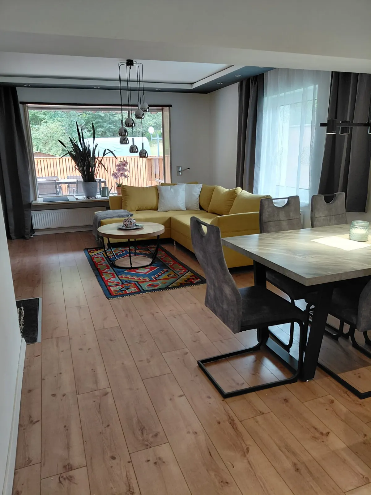 Open-plan living and dining area with dining table, corner sofa and a large window